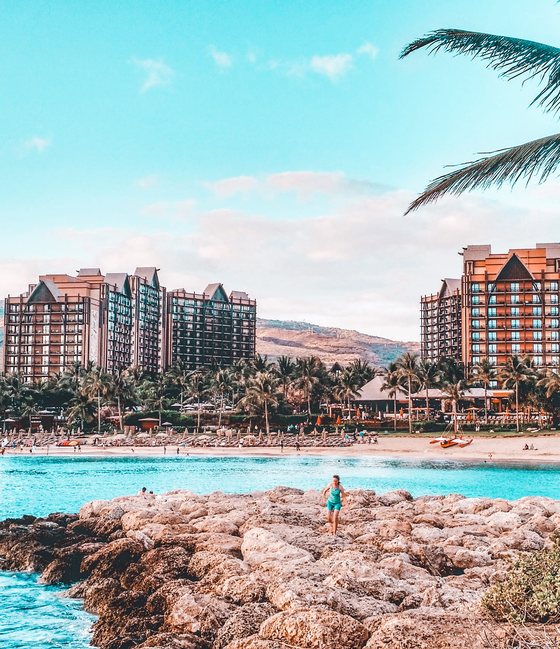 Aulani, A Disney Resort & Spa towers behind a turquoise lagoon and rocky jetty in Ko Olina, Hawaii